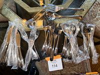 Overview of flatware set including wrapped knives, forks, spoons and serving utensils laid out on a surface.