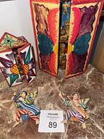 Full view of two folk art nativity sets with colorful painted panels and two separate angel figurines in front.