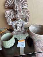 Photo showing the vintage carved statue standing behind two decorative pots on a glass surface against a cardboard background.