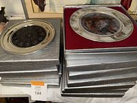 Stack of silver presentation boxes with two pewter-framed plates on top