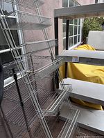 Photo of two tall wire storage shelves with multiple wire racks, chrome finish, standing next to corner balcony wall.