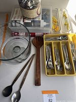 Full view of lot showing flatware in yellow tray, glass bowl, wooden salad utensils, cookie cutters in containers, and plastic decorating syringes at back