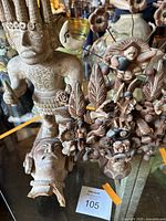 Photo showing the large Aztec male figure, a separate sculpted head, and the Tree of Life statue with figures and flowers.