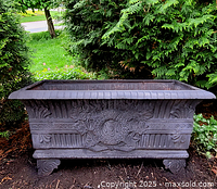 Full front view of rectangular cast iron planter on ground between shrubs