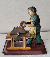 Front angle of antique German tin litho wind-up toy showing man operating grinding wheel on rectangular base.