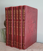 Side view showing seven leather-bound books with gold embossed text and numbers on spine.