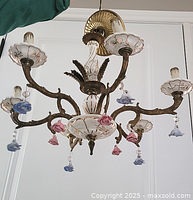 Front view of chandelier showing brass arms, porcelain bobeches, and rose pendants