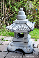 Side view of one concrete garden pagoda sculpture showing detailed tiled roof and ornamental finials with weathered paint.