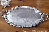 Full top view of oval tray on wooden surface showing ornate border, handles and engraved center