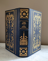 Front and back cover with spine visible showing leather binding with gold embossed intricate designs and book title/author on spine.