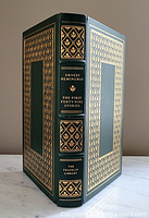 Front cover and spine view showing dark green leather with extensive 22 karat gold embossing and raised spine hubs. Title and author clearly visible.