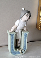 Side view of figurine showing girl leaning on letter U from left side