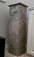 Full height view of the marble pedestal showing square column with speckled pink and black granite finish placed near wall and furniture.