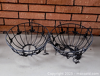 Two black metal hanging basket frames with leaf decorative accents and hanging chains.