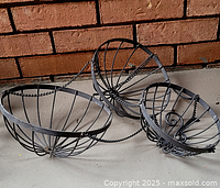 Photo showing all three metal hanging basket frames together on a concrete floor with brick wall background