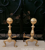 Front view of the pair of brass fireplace andirons placed in front of fireplace screen.