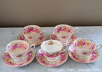 Five Royal Albert Serena pattern teacups and matching saucers arranged on a marble surface, showing floral design and gold trim