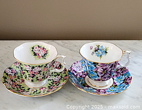 Two Royal Albert floral pattern tea cups with matching saucers showing different floral designs and gold trim; set on marble surface.