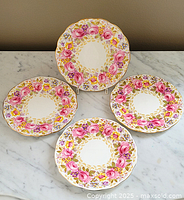 Four Royal Albert Serena floral plates arranged on a marble surface, showing full set with floral pattern and scalloped gold edges.