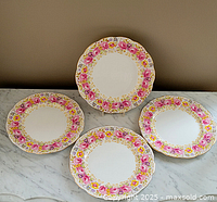 Four Royal Albert Serena 9-inch dinner plates arranged on a marble surface, showing floral and gold detailing.