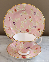 Tea cup, saucer, and dessert plate displayed from side angle showing floral pattern and gold trim.