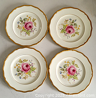 Four Royal Doulton Curnock dinner plates arranged in a square showing floral center with pink rose and gold scalloped rim.