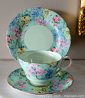 Front view of the teacup on the saucer with the dessert plate displayed behind, showing the floral pattern and gold trim.