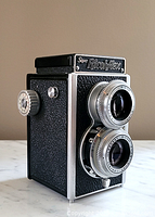 Side/angled view of the Super Ricohflex TLR camera showing black textured body, metal details, and focusing knob.