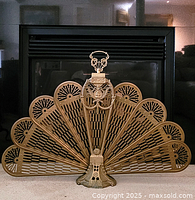 Full view of vintage brass peacock fireplace screen with a fan of perforated brass panels and a detailed central handle.