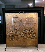 Front view of vintage brass fireplace screen showing detailed embossed medieval scene with knight on horse and townspeople in front of buildings.