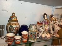Wide view of top shelf showing entire lot including mini cups, ginger jars, figurines and ornate vase on glass shelf