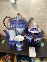 Full set of two larger teapots, one smaller teapot, and one mug on shelf.