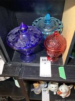 Photo showing three colored glass candy dishes: light blue spooner sugar dish, purple pedestal candy dish, and red candy dish with lids and floral patterns.