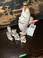 Photo showing the fish-shaped ceramic decanter with gold spherical stopper and all five matching fish-shaped cups grouped together.
