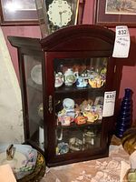 Front-right angled view of a small dark wood display cabinet with glass front door showcasing a variety of small decorative items inside.