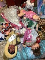 Photo showing multiple dolls including Cabbage Patch Kids, porcelain dolls, and stuffed bear, displaying clothing details and facial features.