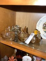 Four glass animal figurine containers displayed on a wooden shelf, including a clear swan, two clear ducks, and an amber hen on nests, showing overall set.