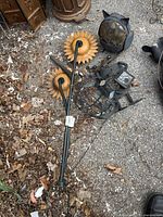 Photo showing large metal sunflower garden stake, metal lantern frame, and metal frog hanging decor on ground with leaves.