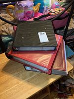 Three binders stacked on a wooden table, one black on top of two red binders, showing their covers and spines.