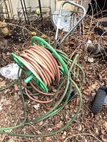 Full view of green metal hose reel cart with orange hose wound, green hose loose on ground.