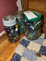 Three jars with a mixture of vintage glass marbles inside including colored and patterned marbles.