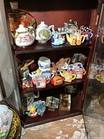 Shelf with multiple miniature teapots and small collectible figurines arranged closely together including animal and house-themed teapots