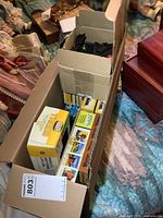 Box with multiple boxes of model train track pieces and model cars visible inside, taped cardboard box.