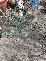 Overhead photo showing four green metal plant stands arranged together on a paved surface outdoors, with a blue flower-shaped garden decor piece and other small garden decorations visible nearby.
