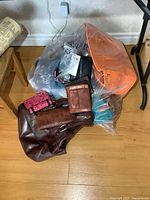 Photo showing assortment of purses and wallets inside a plastic bag on wooden floor with wall outlet visible.