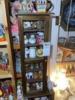 Wooden display cabinet filled with various salt and pepper shakers, capturing overall appearance and shelving arrangement.