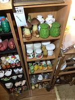 Front view of wooden open display shelf filled with salt and pepper shakers of various styles including mushrooms, owls, apples, and other shapes.