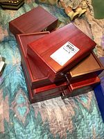Stack of nine small wooden trinket boxes, reddish wood with hinged lids, grouped together on quilted fabric.