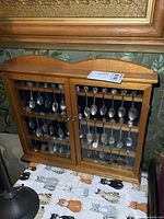 Front view of wooden spoon display case with glass doors closed showing spoons.