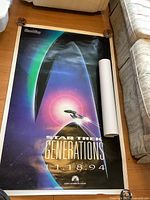 Photo of Star Trek Generations poster rolled next to a couch on wooden floor. Bright colors with spaceship image and release date.